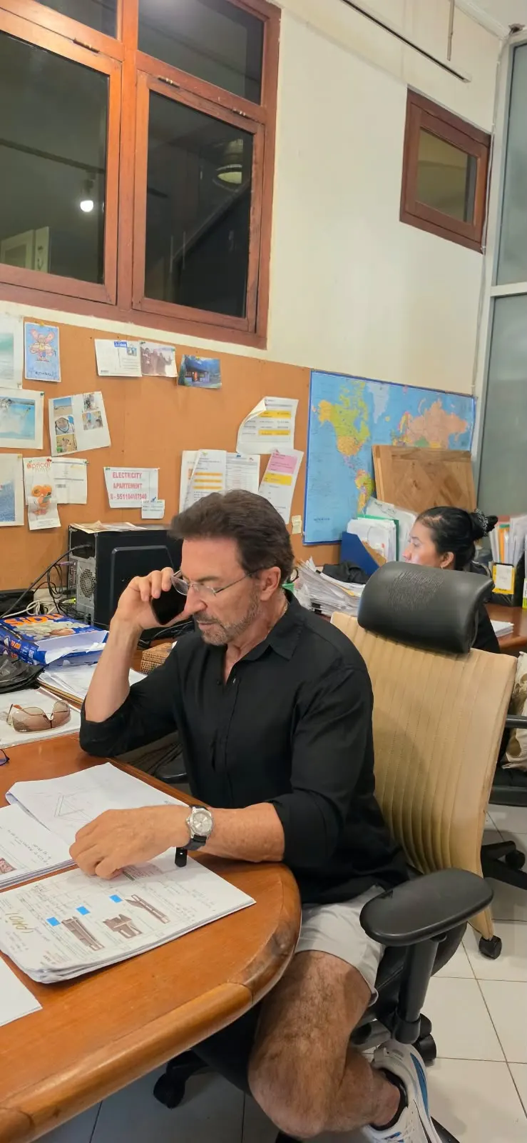 Alain au téléphone à son bureau de Bali, plans de fabrication en main